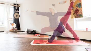A yoga studio with wooden flooring, yoga mats, and a wall with a decorative tapestry.