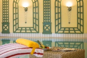 Una habitación con una cama, un frutero y una revista sobre un otomano tejido.