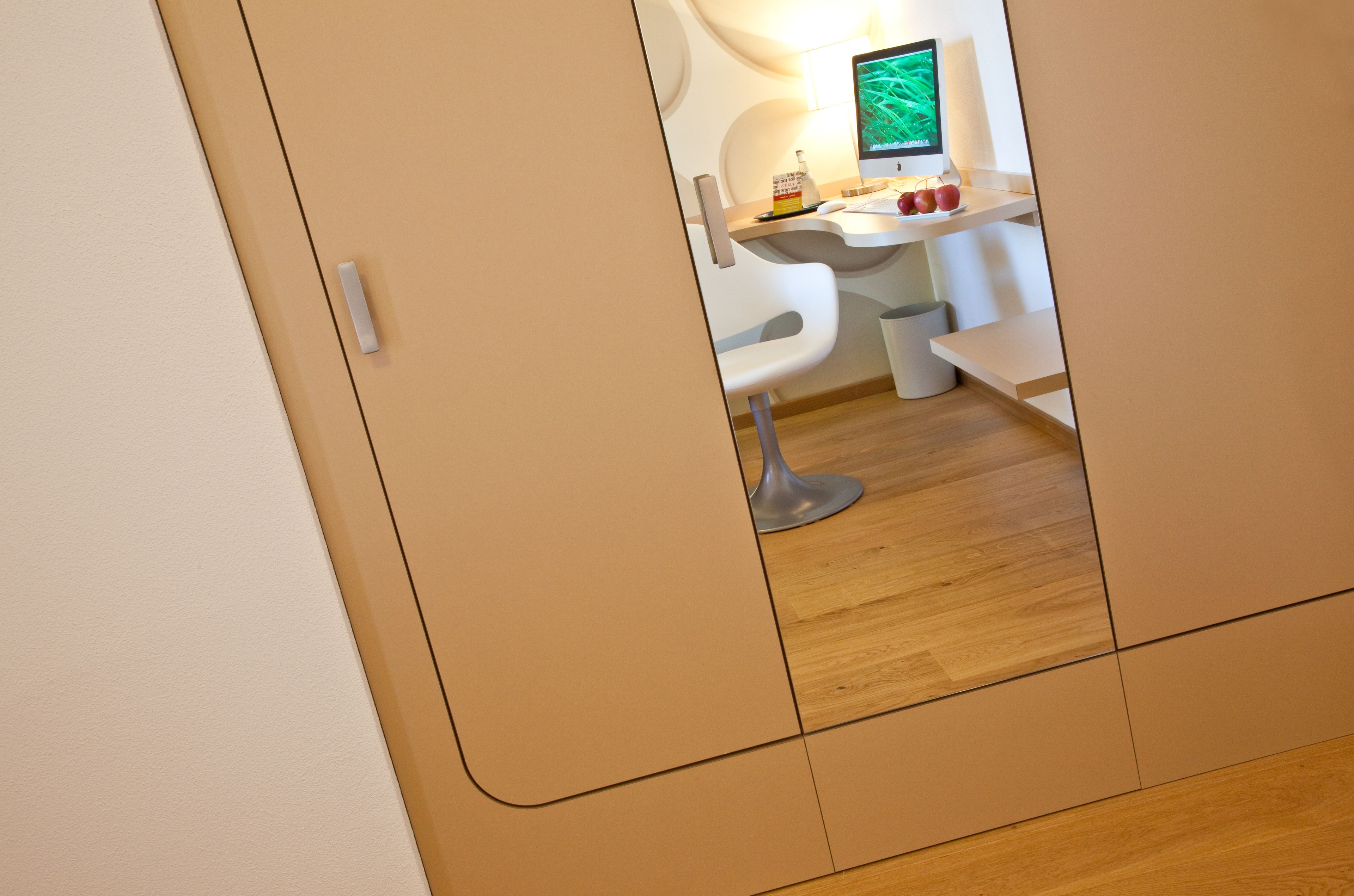 A modern, minimalist room with a wooden floor, a white desk, and a computer monitor.