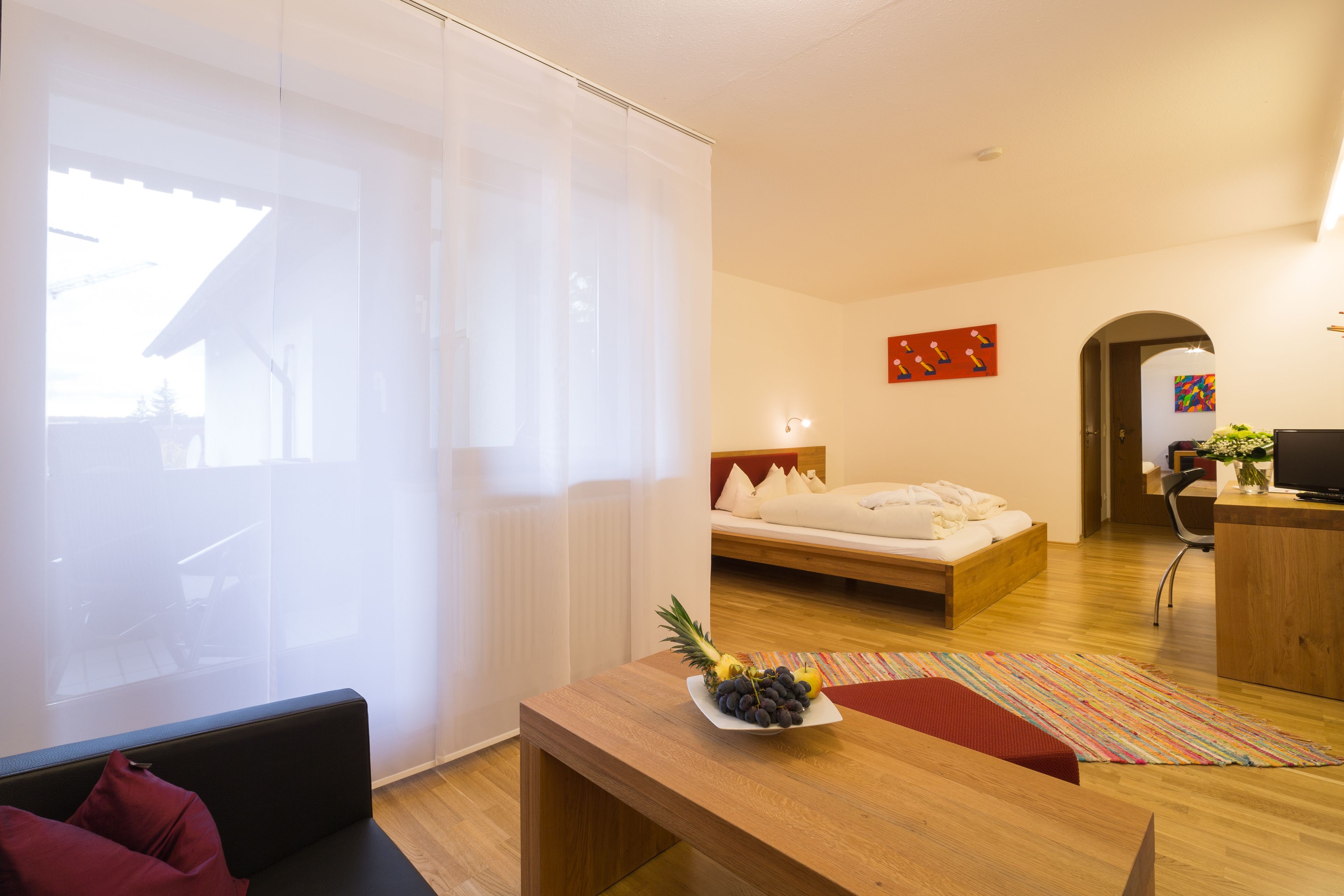 A modern hotel room with a bed, a wooden desk, and a sofa.