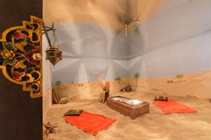 Una habitación con decoración de estilo desértico, que incluye un suelo color arena, un farol colgante y una pequeña mesa cubierta con un paño rojo.