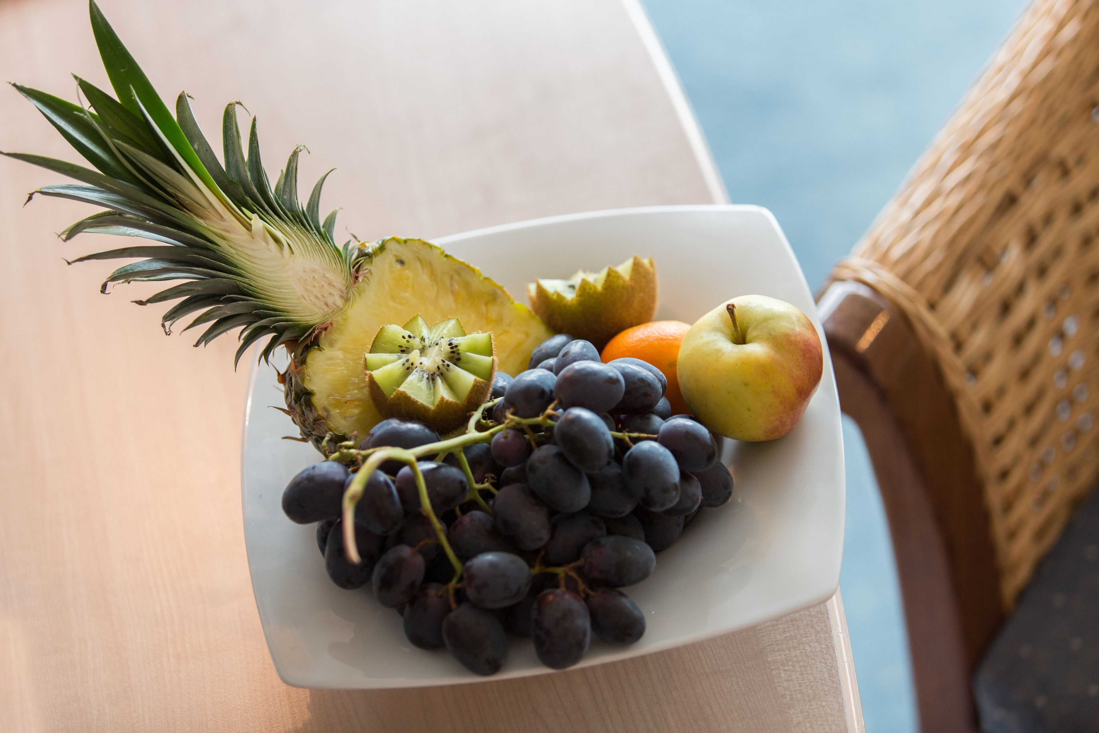 A plate of fruits including grapes, pineapple, apple, and orange on a table.