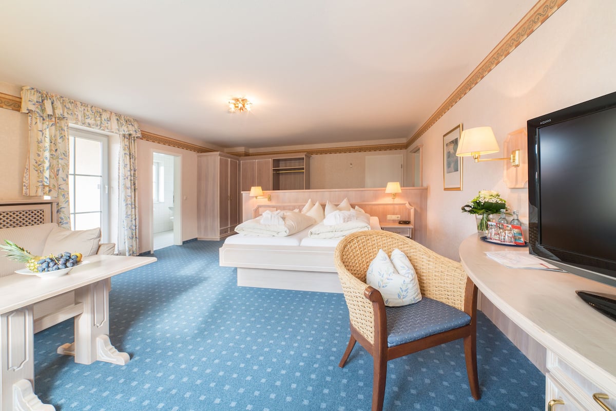 A hotel room with a bed, a seating area with a chair, a desk, a television, and a window with curtains.