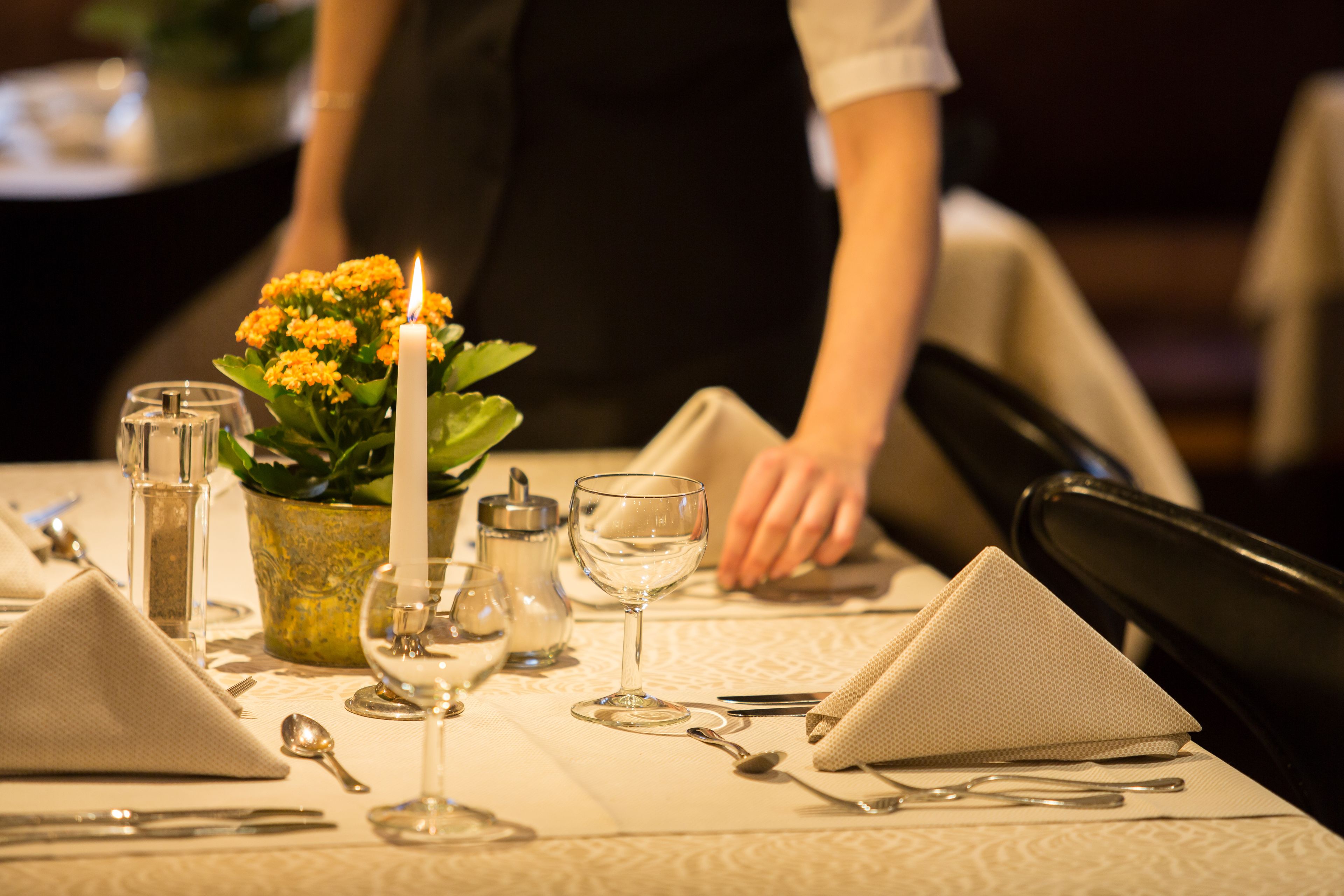 Une table mise pour le dîner, avec une bougie, de la verrerie et une petite plante.