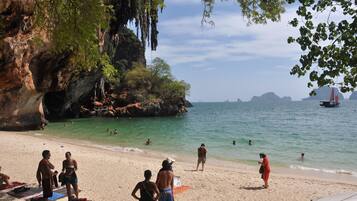 A beach with people swimming and sunbathing, a rocky cliff, and a boat in the distance.