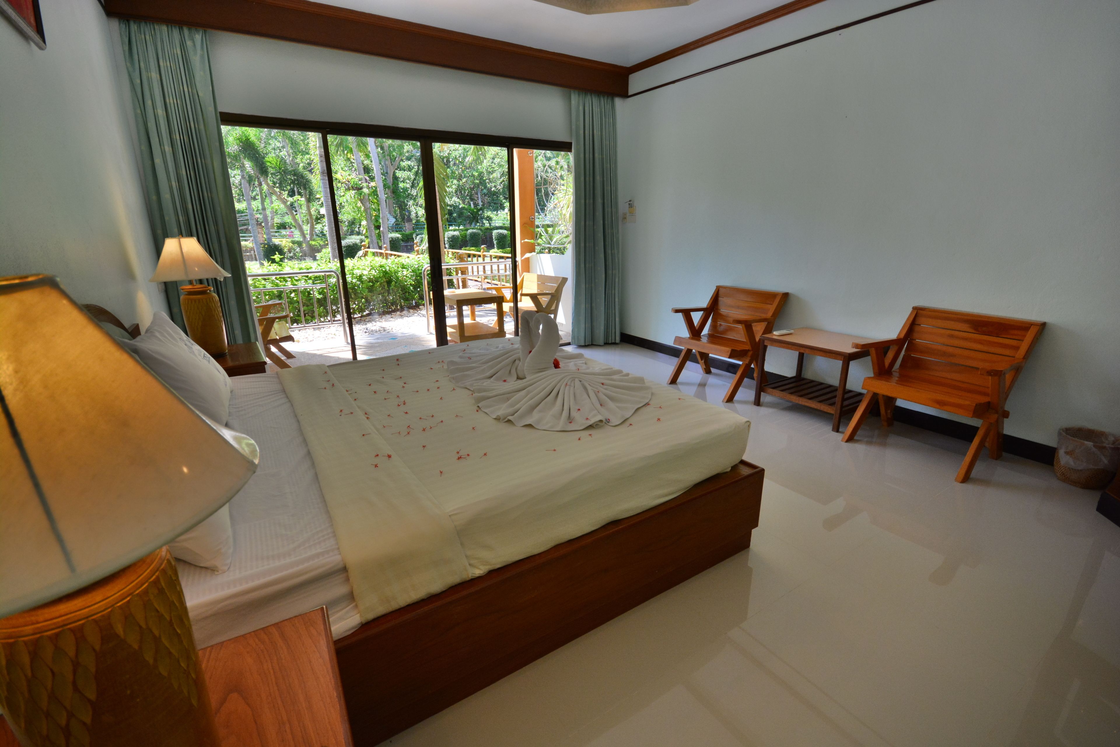 Une chambre d’hôtel dotée d’un grand lit, d’un coin salon avec une table et des chaises, et offrant une vue sur un jardin grâce à une porte coulissante.