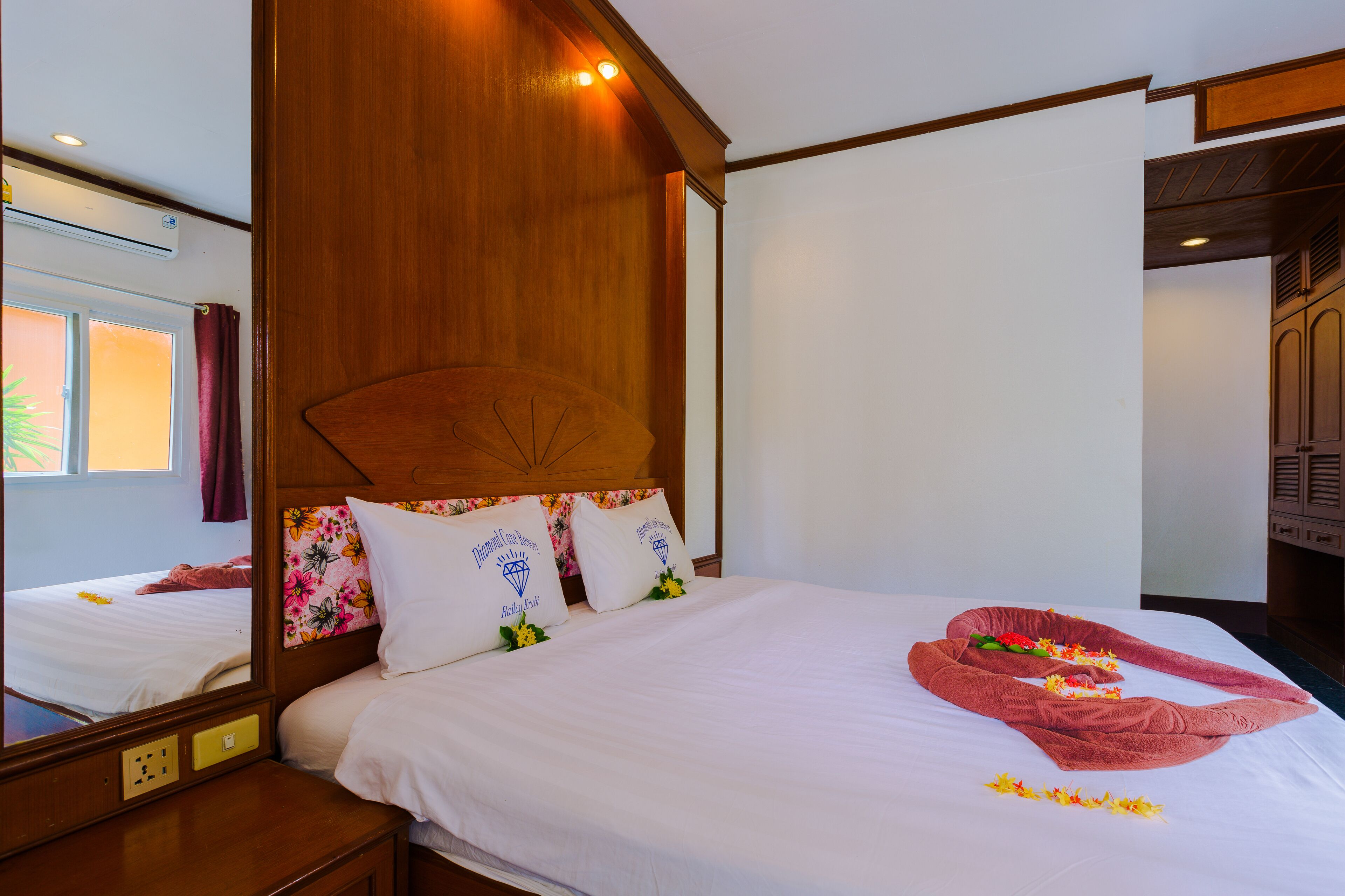 A hotel room with a wooden headboard, a large mirror, and a neatly made bed with floral pillows and a towel arrangement.
