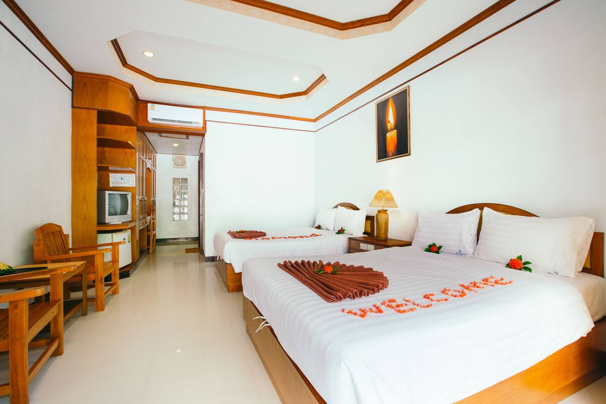 Habitación de hotel con dos camas, televisión, muebles de madera y techo con diseño geométrico.