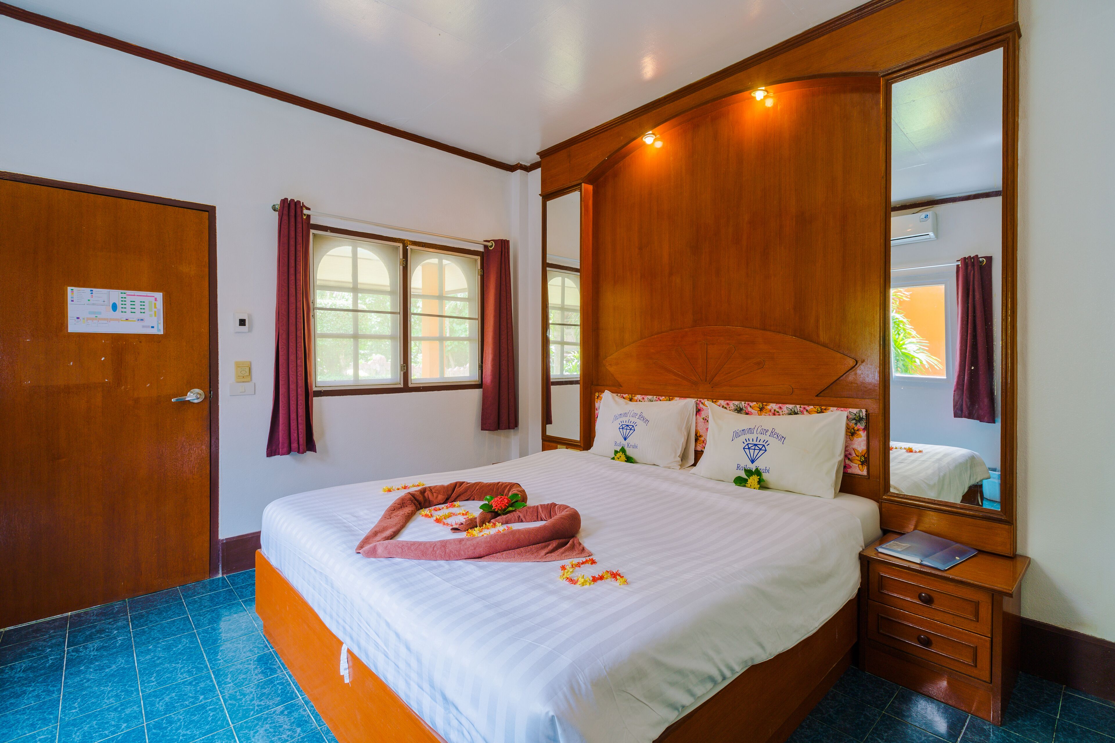 Habitación de hotel con una cama grande, cabecera de madera, mesita de noche, espejo y ventana con cortinas.