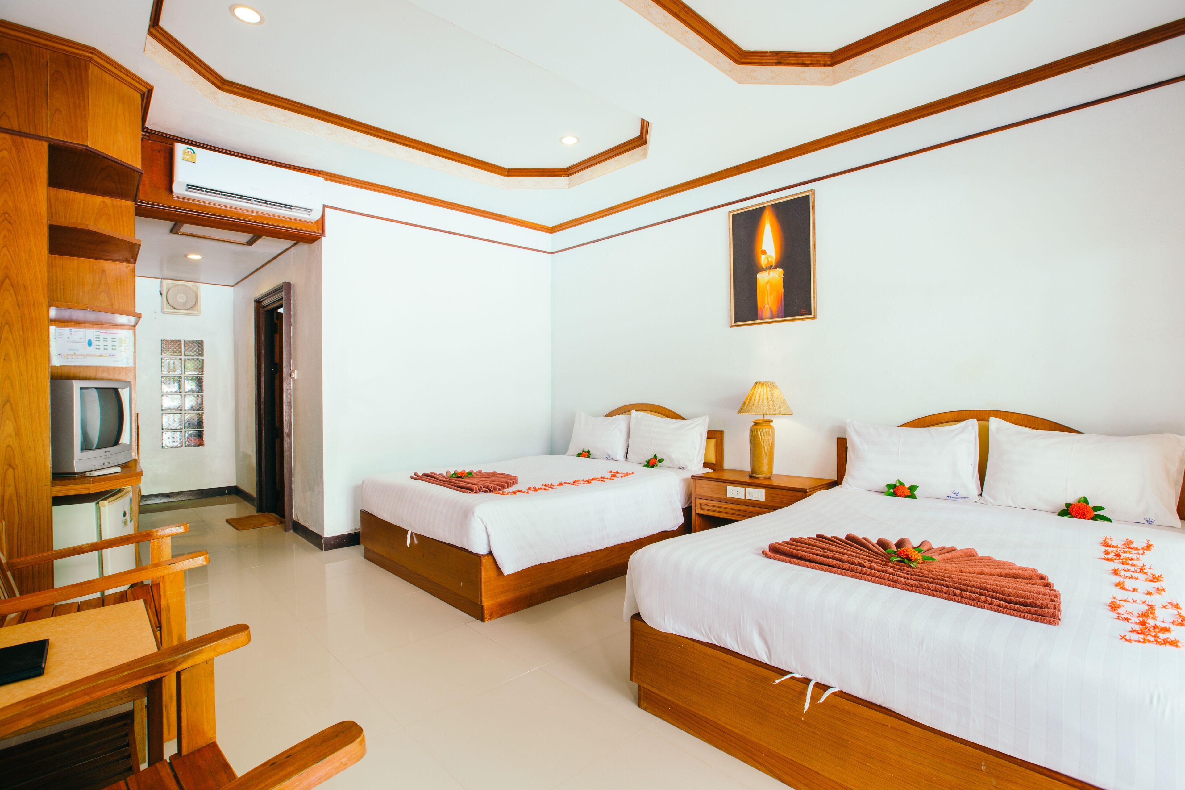 A hotel room with two beds, wooden furniture, a television, and a wall-mounted air conditioner.