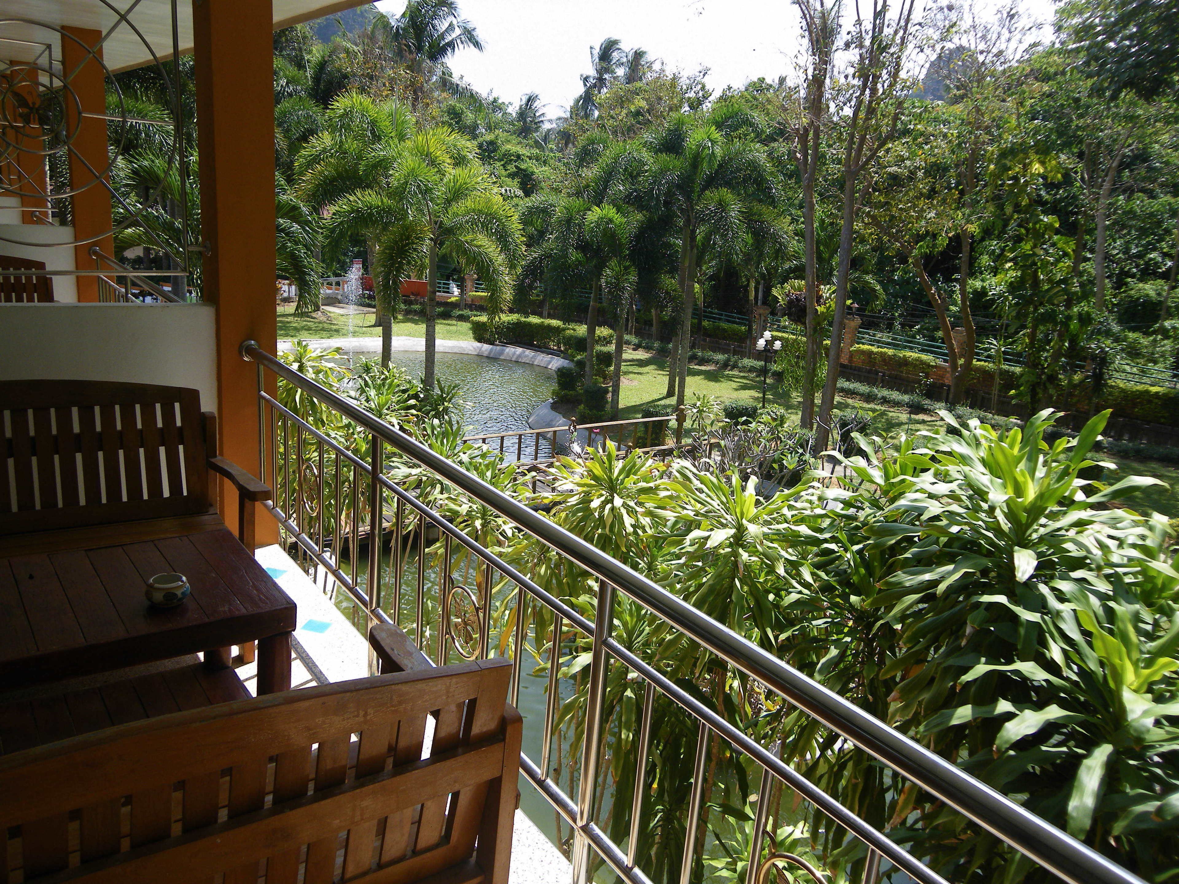Un balcone con una panca e un tavolo di legno, con vista su un giardino con diverse piante e un piccolo stagno.