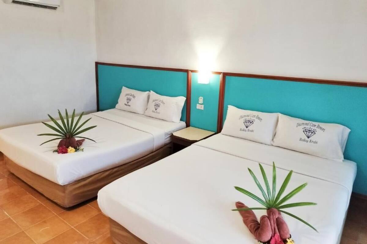 Habitación de hotel con dos camas individuales, cada una con colchón blanco y cabecero color turquesa.