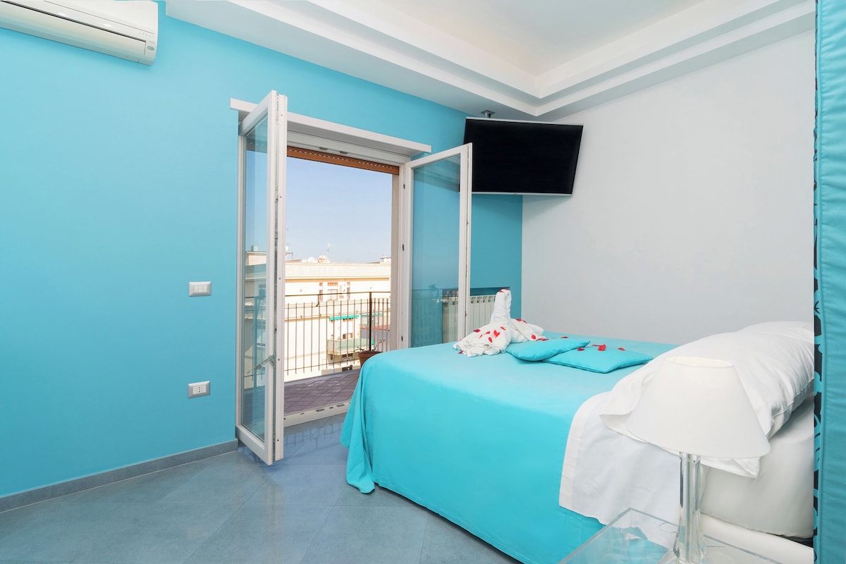 A bedroom with a bed, a TV mounted on the wall, and a balcony door.