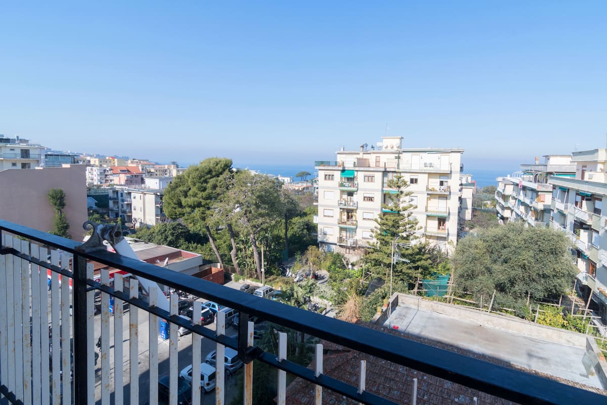 A multi-story residential building with balconies, a view of the sea, and a clear sky.