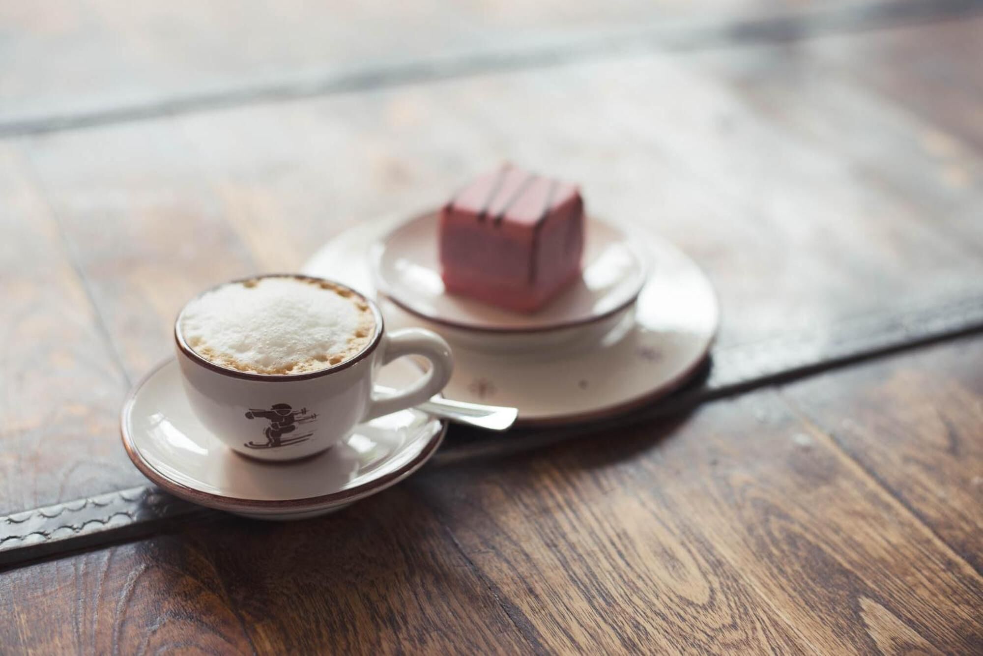 Eine Tasse Kaffee mit Schaum auf einem Untertasse und ein kleines, pinkes Würfelchen auf einem passenden Untertasse.