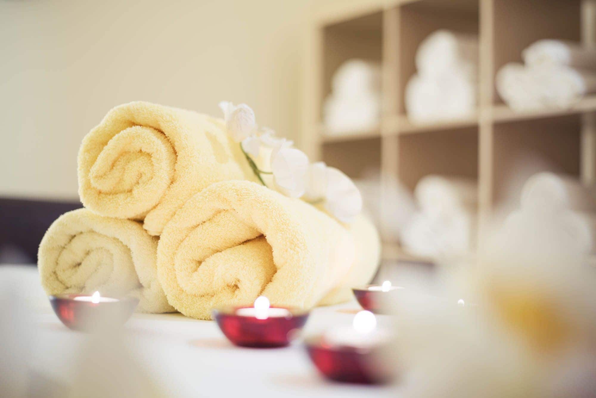 Neatly rolled towels stacked on a table, with candles and white flowers nearby.