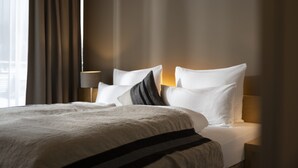 A hotel room with a neatly made bed, a bedside lamp, and a view of the city through the window. - Skihotel Galzig (Sankt Anton am Arlberg)