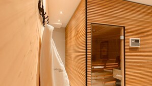 A modern hotel room with a wooden panel design, a glass door leading to a bathroom, and a visible towel hanging on the wall. - Skihotel Galzig (Sankt Anton am Arlberg)