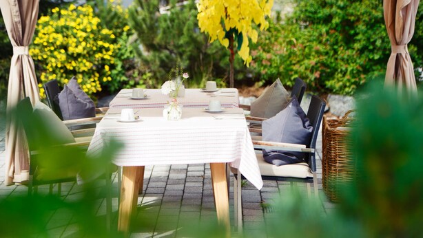 An outdoor dining area with a table set for four, surrounded by chairs and a wicker basket. - Skihotel Galzig (Sankt Anton am Arlberg)