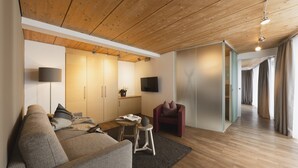 A modern living room with a wooden ceiling, a sofa, a red chair, a small table, and a TV mounted on the wall. - Skihotel Galzig (Sankt Anton am Arlberg)