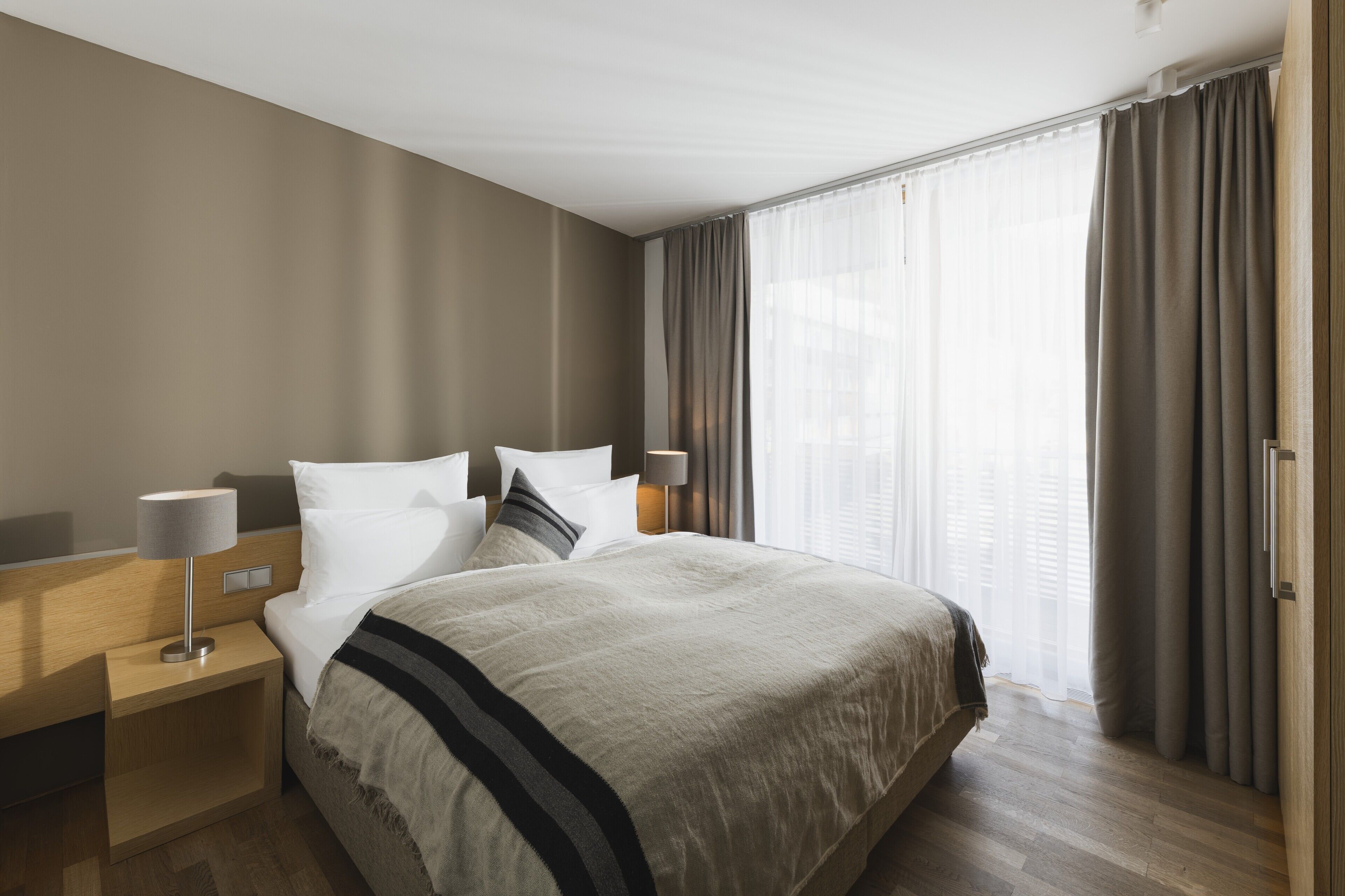 Een hotelkamer met een bed, nachtkastjes, een lamp en een raam met gordijnen.