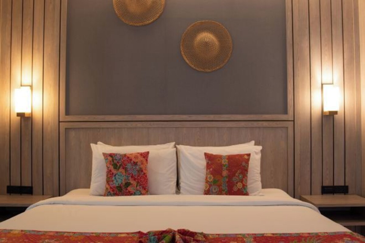 A hotel room with a bed, two wall-mounted lamps, and two decorative wall hangings.