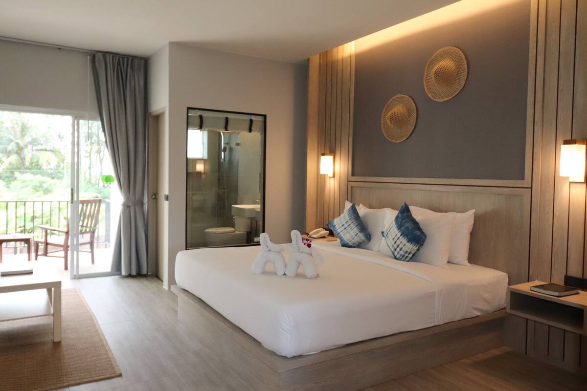 Een hotelkamer met een groot bed, een bureau en een stoel. Er is een balkon met uitzicht op groen.