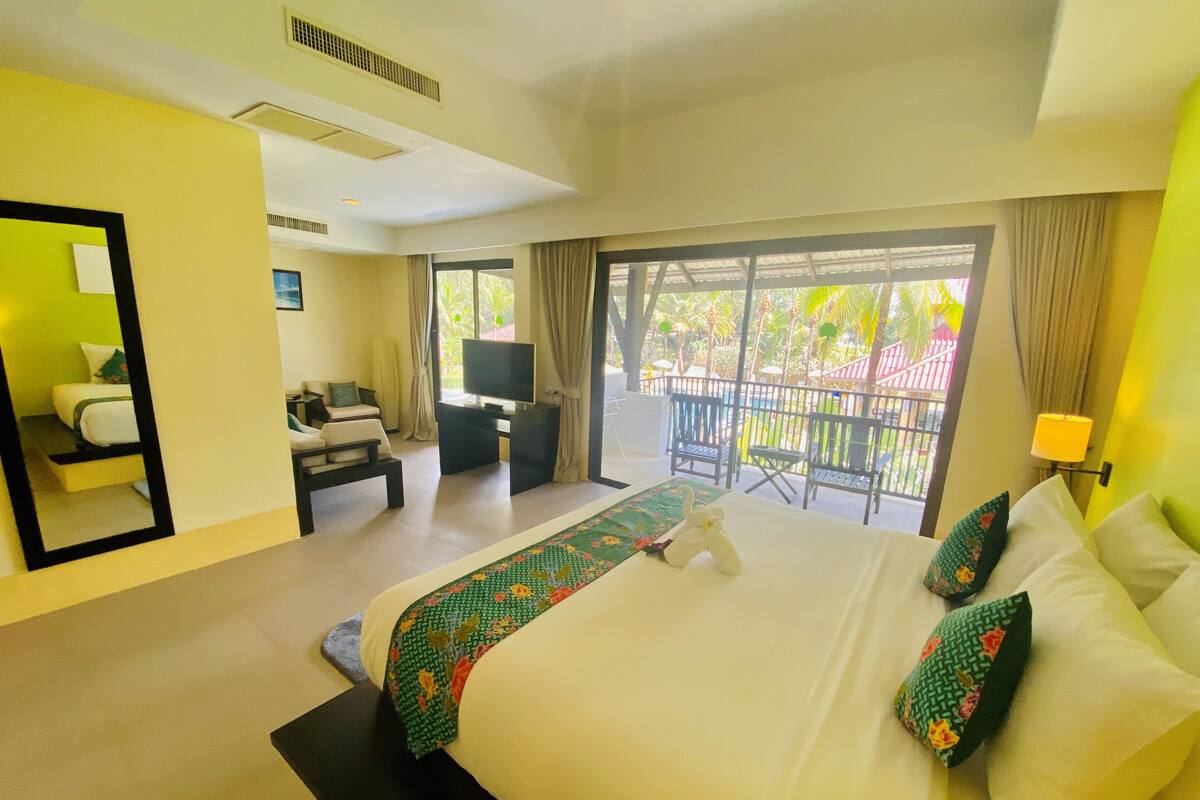 Hotelkamer met een groot bed, een televisie, een bureau en een balkon met uitzicht op palmbomen.