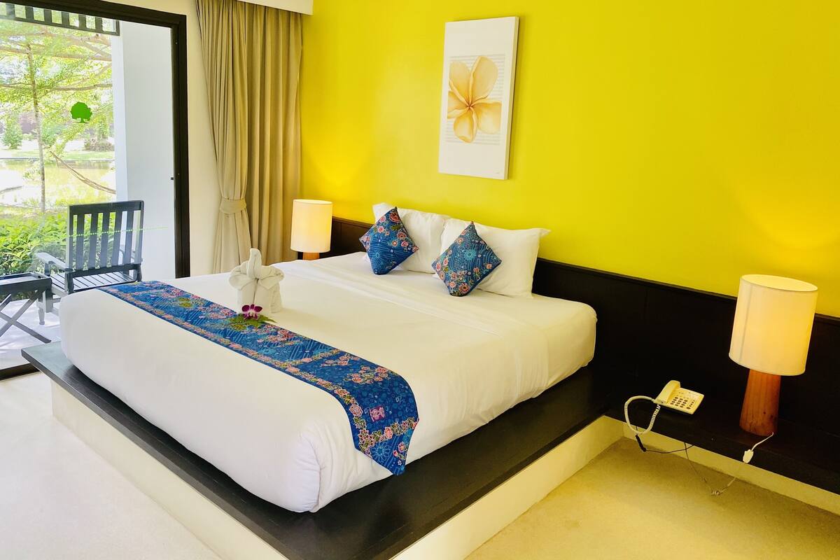 Een hotelkamer met een bed, twee bedlampen, een raam met gordijnen en een stoel.