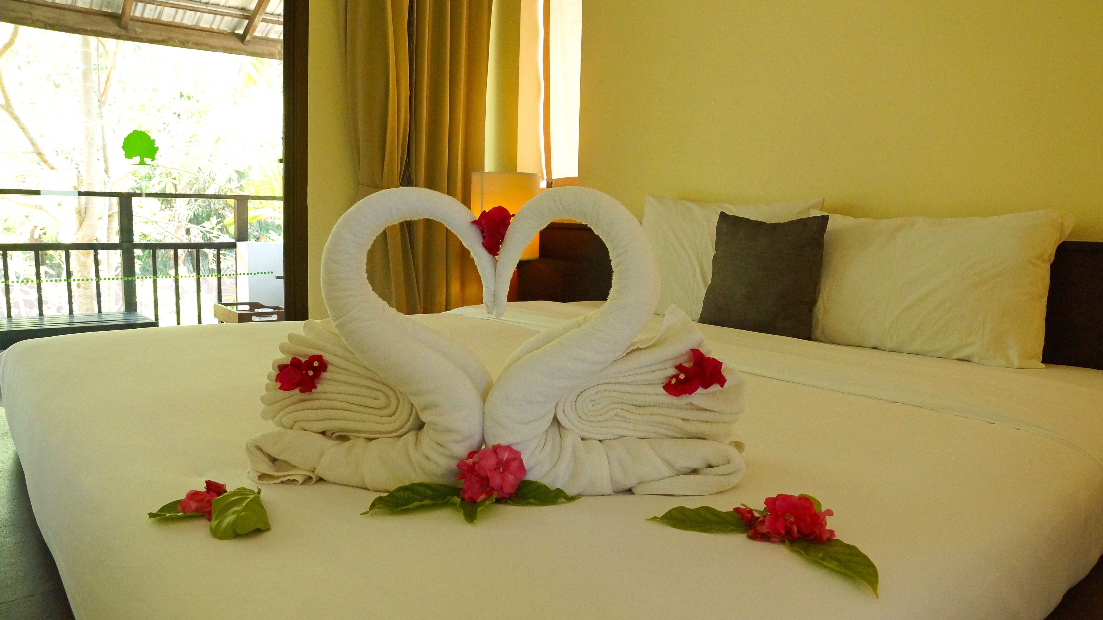 Una cama con un arreglo de toallas decorativo con forma de cisne y flores.