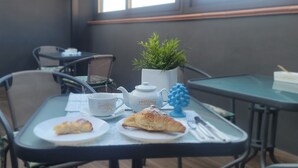 Uma mesa com uma xícara branca, um objeto decorativo azul, uma pequena planta e um prato com um pastel.