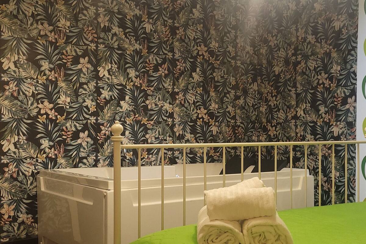 A bedroom with a green quilted bedspread, a white radiator, and floral wallpaper.