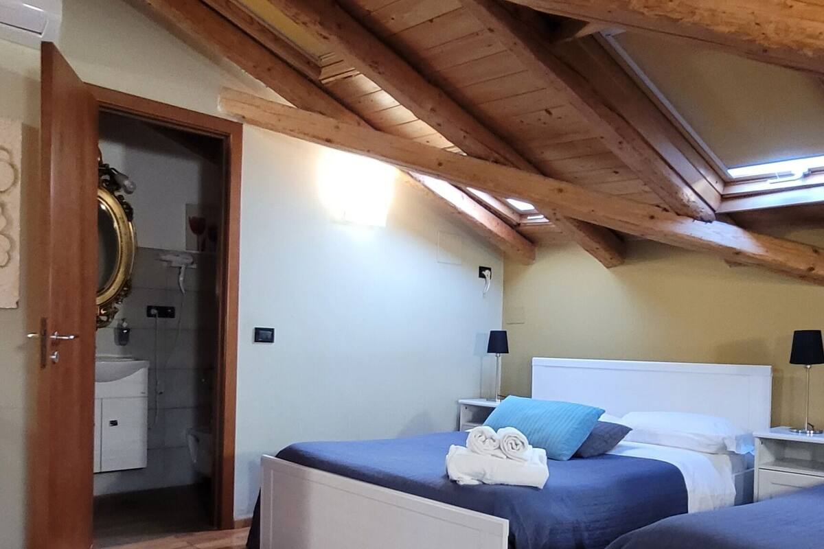 A room with two beds, wooden flooring, and a sloped ceiling.