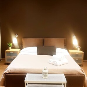 A neatly made bed with a pillow, two bedside tables with lamps, a small table with a lantern, and a potted plant on one of the tables. - XX Miglia (Catania)