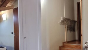 Quarto com soalho de madeira, um guarda-roupa branco e uma escadaria que leva a outra área.