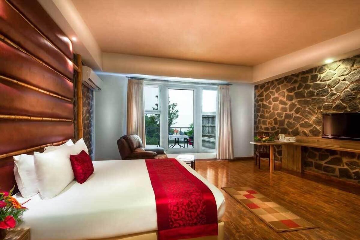 A hotel room with a large bed, a stone wall, a television, and a balcony with a table and chairs.