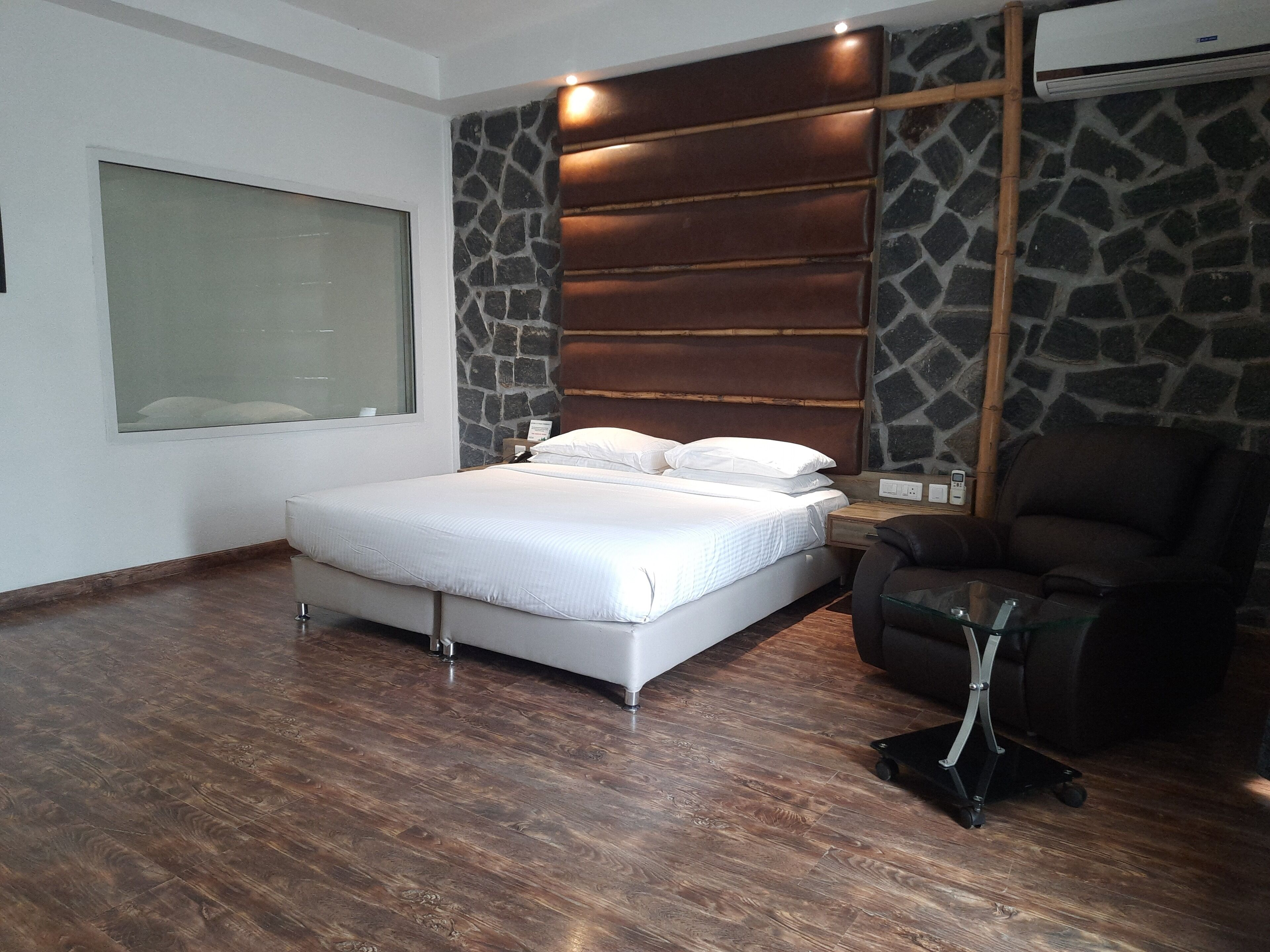 A bedroom with a large bed, a chair, a massage table, and a stone wall.