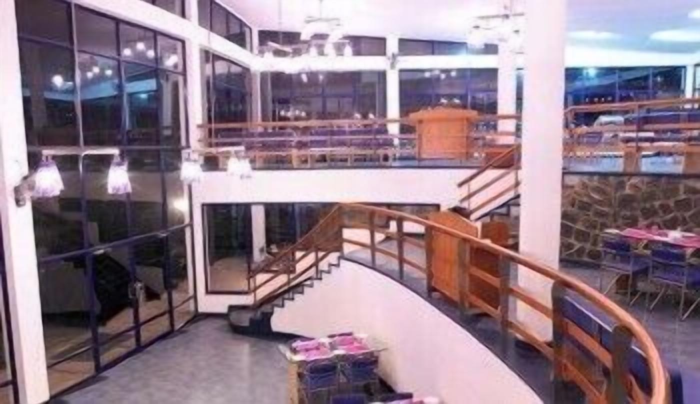 A modern hotel lobby with a curved staircase, large windows, and a seating area with tables and chairs.