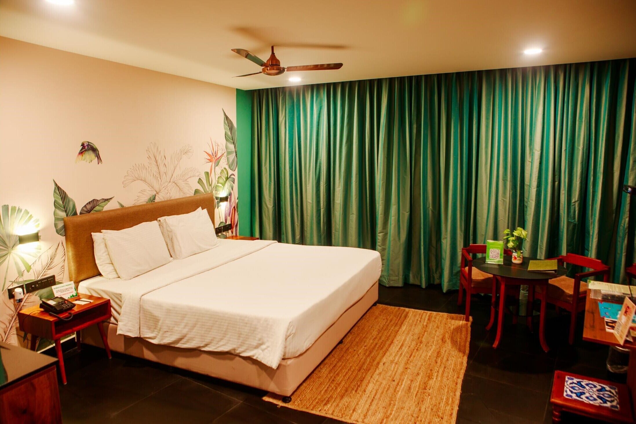 Una habitación de hotel con cama, escritorio, silla, mesa, ventilador de techo y cortina verde.