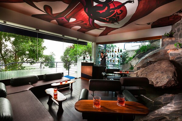 Un área de descanso moderna con pared de piedra, muebles de madera y un gran mural abstracto en el techo.
