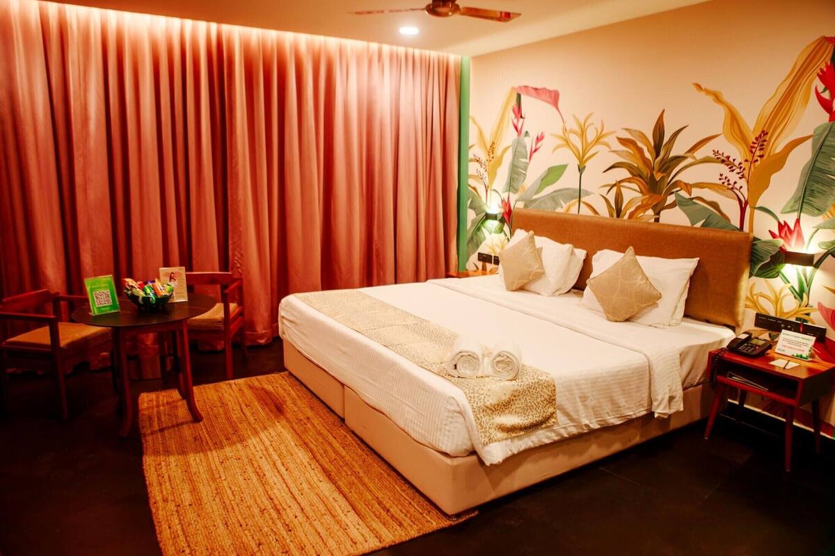 A hotel room with a large bed, a desk, chairs, and a tropical-themed wall mural.