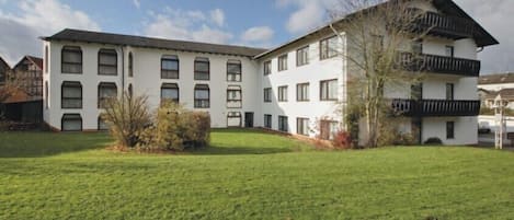 A two-story building with a flat roof, multiple windows, and a small garden area in front.