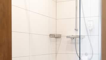 Een douche met glazen wanden, betegeld met witte tegels, met een handdouche en een bedieningspaneel aan de muur.