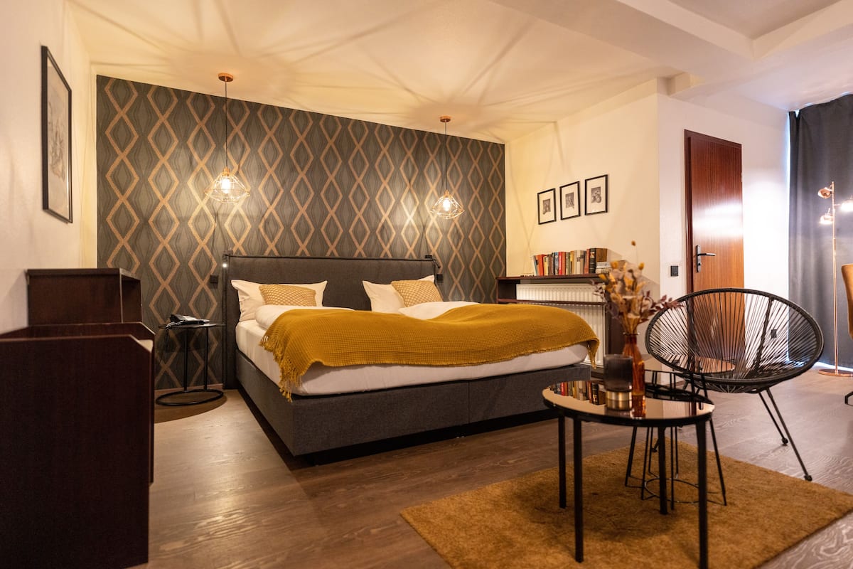 A modern bedroom with a large bed, a side table, a chair, and a bookshelf.