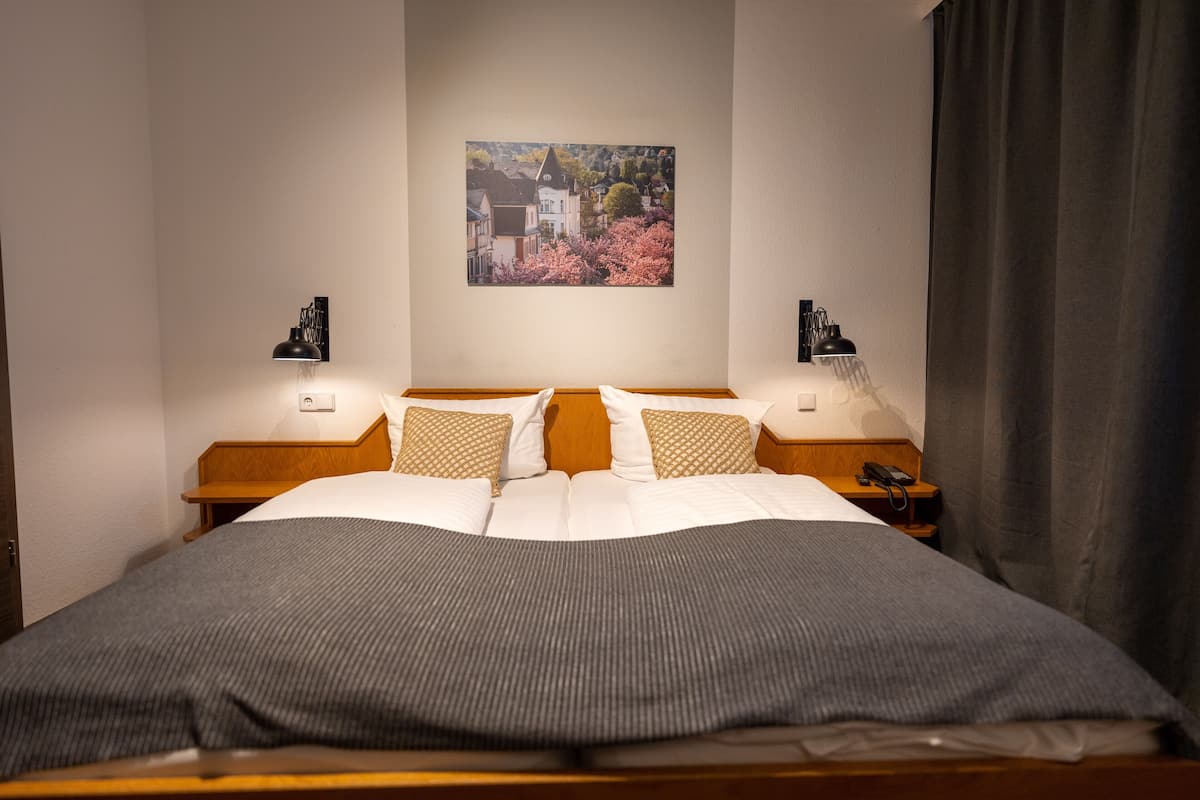 A neatly made bed with a gray blanket, two bedside lamps, a framed picture on the wall, and a wooden nightstand with a phone.