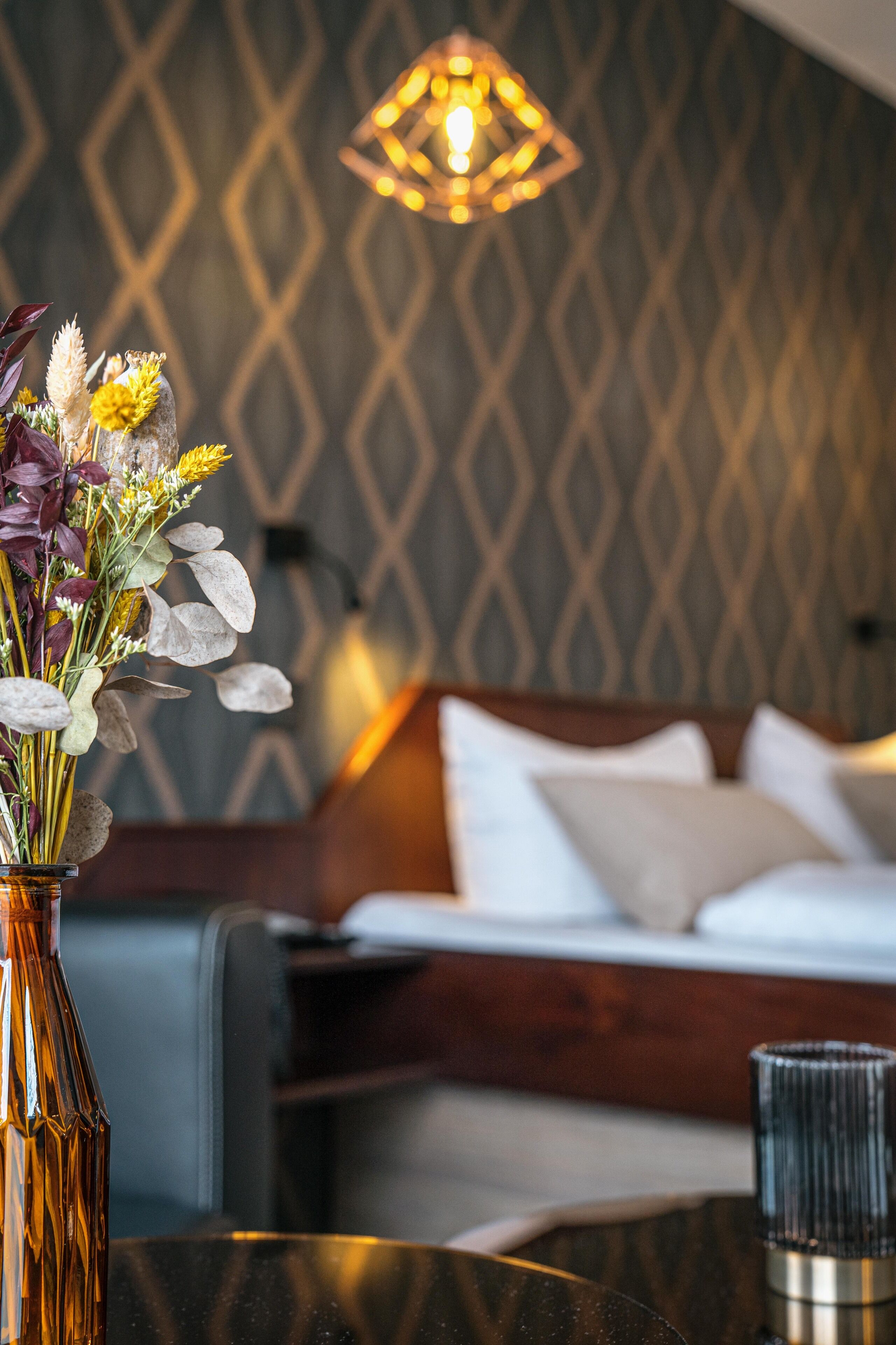 Ein Hotelzimmer mit einem Bett, einem Nachttisch mit Blumenvase und einer Wand mit Muster.