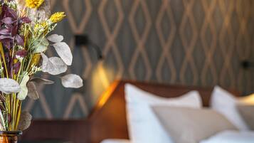 Ett hotellrum med en säng, ett nattduksbord med en vas med blommor och en vägg med ett mönster.