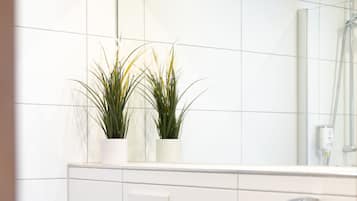 Une salle de bain moderne avec des toilettes, un lavabo et un miroir. Deux plantes en pot sont posées sur le mur au-dessus des toilettes.