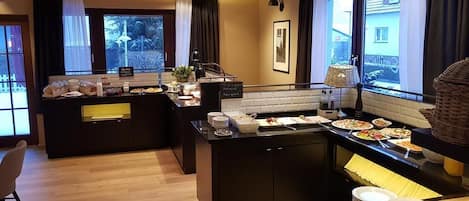 Cocina moderna con una isla central, bufé de desayuno y diversas opciones de comida, y vista al exterior a través de amplios ventanales.