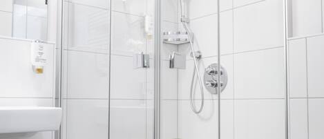 A modern bathroom with a glass-enclosed shower, white tiles, and a visible toilet.